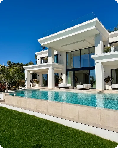 A white villa with an infinity pool and a lawn in front, under a blue sky
