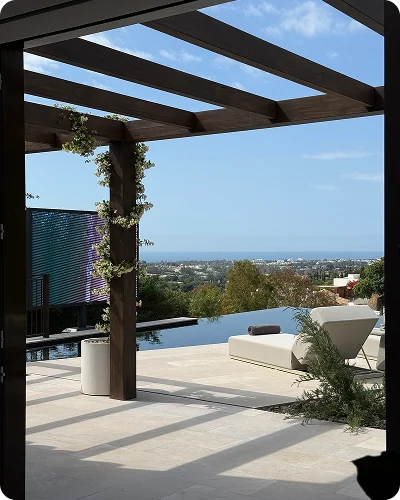A covered terrace with a wooden pergola, a sun lounger and a pool, looking out to the sea